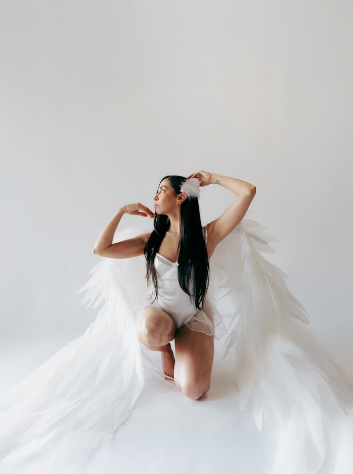 Artistic portrait of a woman in white with large angel wings on a seamless backdrop.