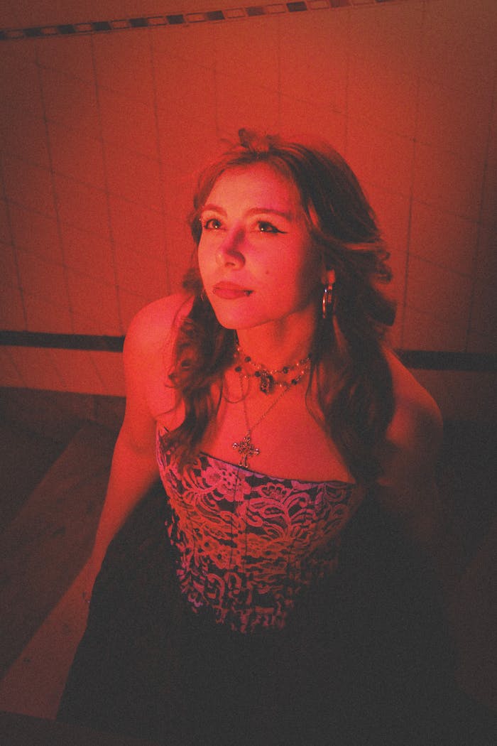 A woman stands confidently in a dimly lit room, bathed in red light.