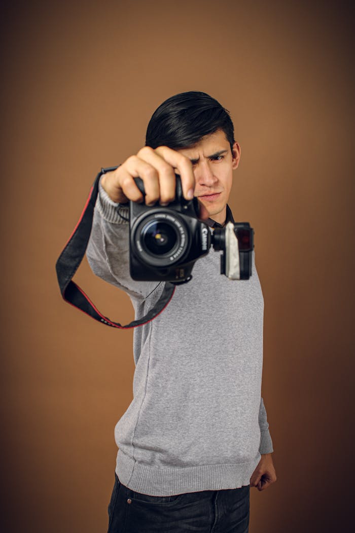 Portrait of a young man holding a DSLR camera, capturing a studio vibe.